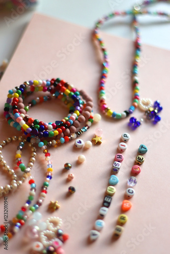 Friendship bracelet spelled with letter beads. Colorful handmade bracelets and various beads. Selective focus, pink background.