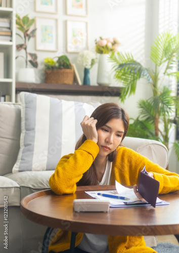 Frustrated young Asian woman looks at her empty wallet with a worried expression, feeling stressed about her financial instability and unpaid loan. Serious Asian woman thinking about financial future.