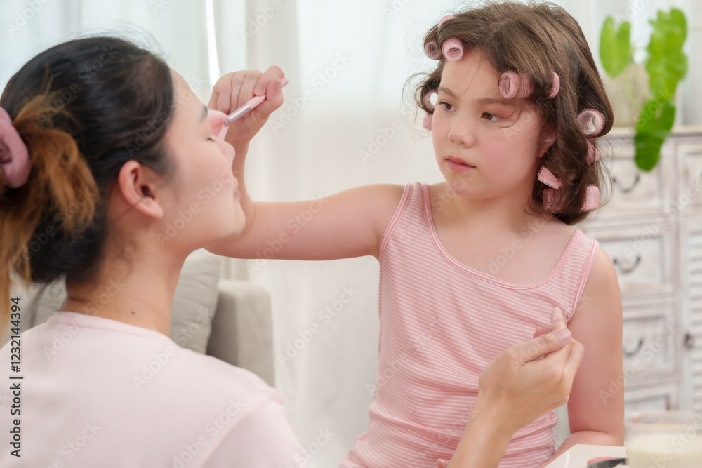 Happiness of Caucasian daughter and Asian mother. Daughter carefully applying blush to mother’s face. Beauty bonding session filled with love and patience. Enjoyable family moment at home. Happiness of Caucasian daughter and Asian mother. Daughter carefully applying blush to mother’s face. Beauty bonding session filled with love and patience. Enjoyable family moment at home.