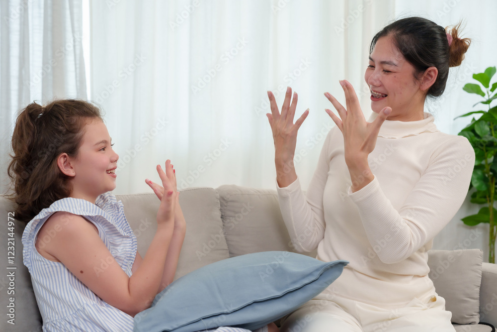 Happiness of Caucasian daughter and Asian mother. Both admiring freshly painted nails with joy. Smiling together in a fun beauty bonding session. Loving and happy family moment at home.
