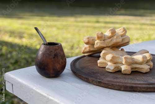 A calabash mate cup with a straw and yerba inside, a South American infusion served with hot water, next to a traditional bread to share on a table in the countryside for breakfast