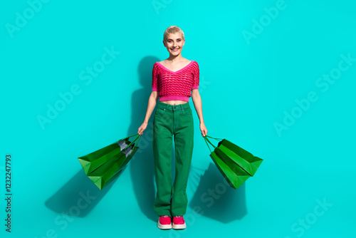 Young woman posing with green shopping bags against teal background in stylish casual clothing photo