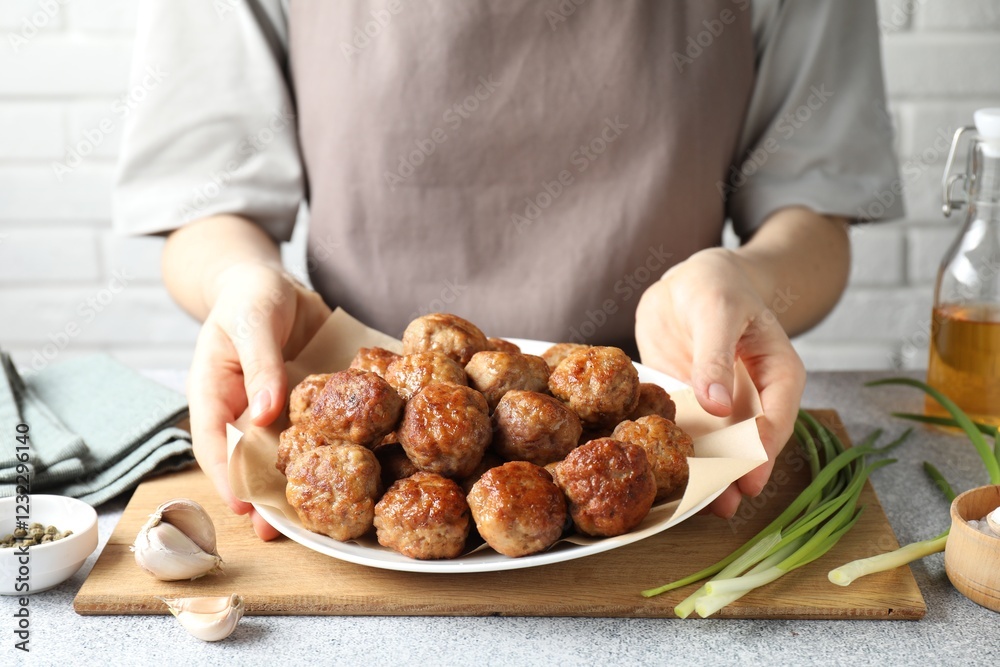 Woman holding plate with delicious meatballs at light textured table, closeup Woman holding plate with delicious meatballs at light textured table, closeup