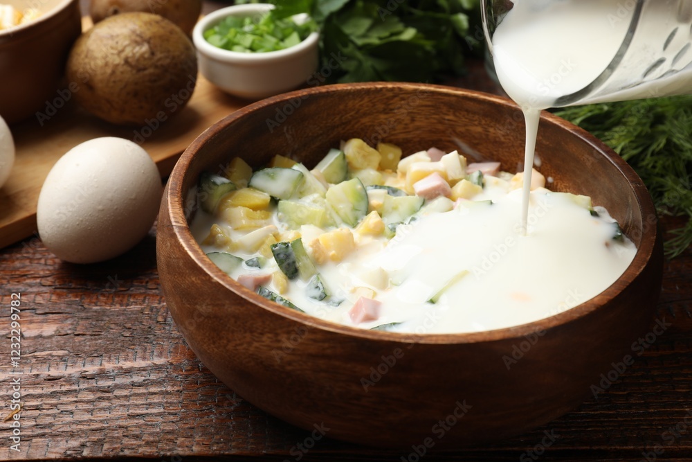 Making okroshka soup. Adding kefir to bowl with ingredients at wooden table, closeup Making okroshka soup. Adding kefir to bowl with ingredients at wooden table, closeup