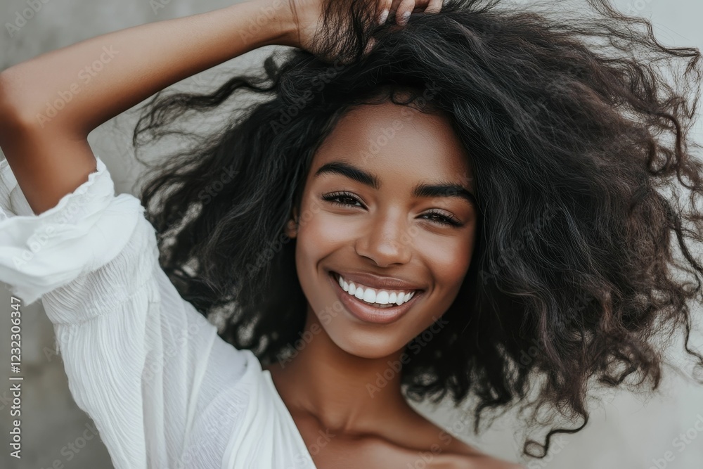 Fototapeta premium Dark haired person smiles brightly, holding their curly hair.