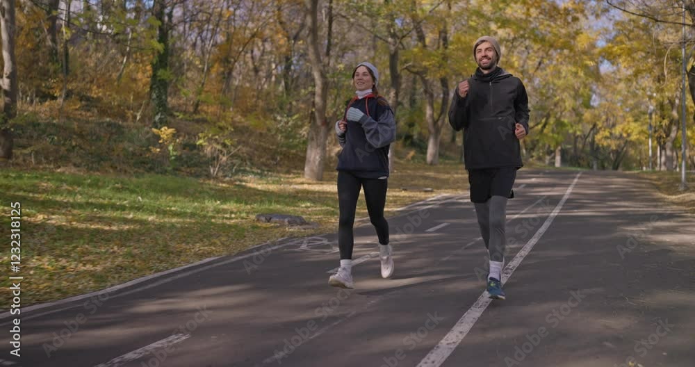 A happy guy in black sportswear runs with his girlfriend along an alley with markings and enjoys an autumn Day in the park A happy guy in black sportswear runs with his girlfriend along an alley with markings and enjoys an autumn Day in the park