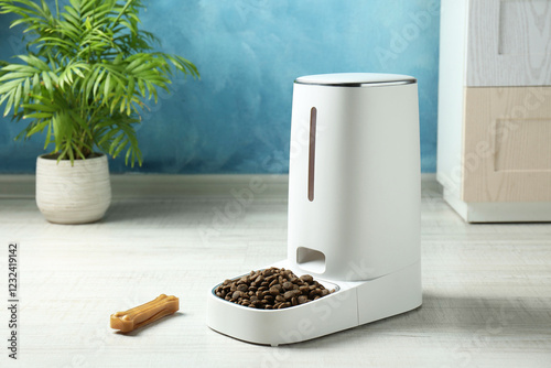 Dry pet food in automatic feeder and chew bone on floor indoors