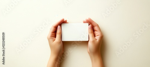 Overhead view of two hands gently holding a blank white card against a creamy beige background with subtle texture. The image evokes a sense of