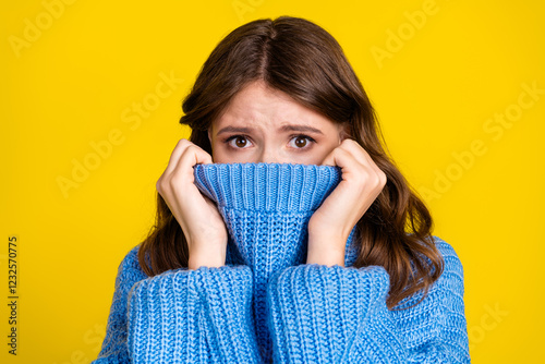 Portrait of a young woman with a surprised look wearing a blue sweater against a vibrant yellow background. photo