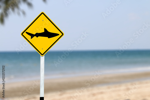 A bright yellow warning sign with a shark symbol, alerting beachgoers to avoid swimming in the area due to potential shark danger, ensuring public safety.