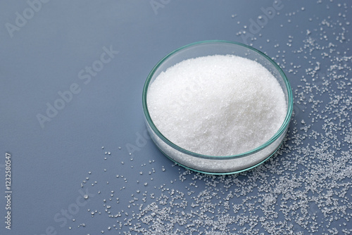 Foto White caster sugar in a petri dish and around, blue background, copy space for text