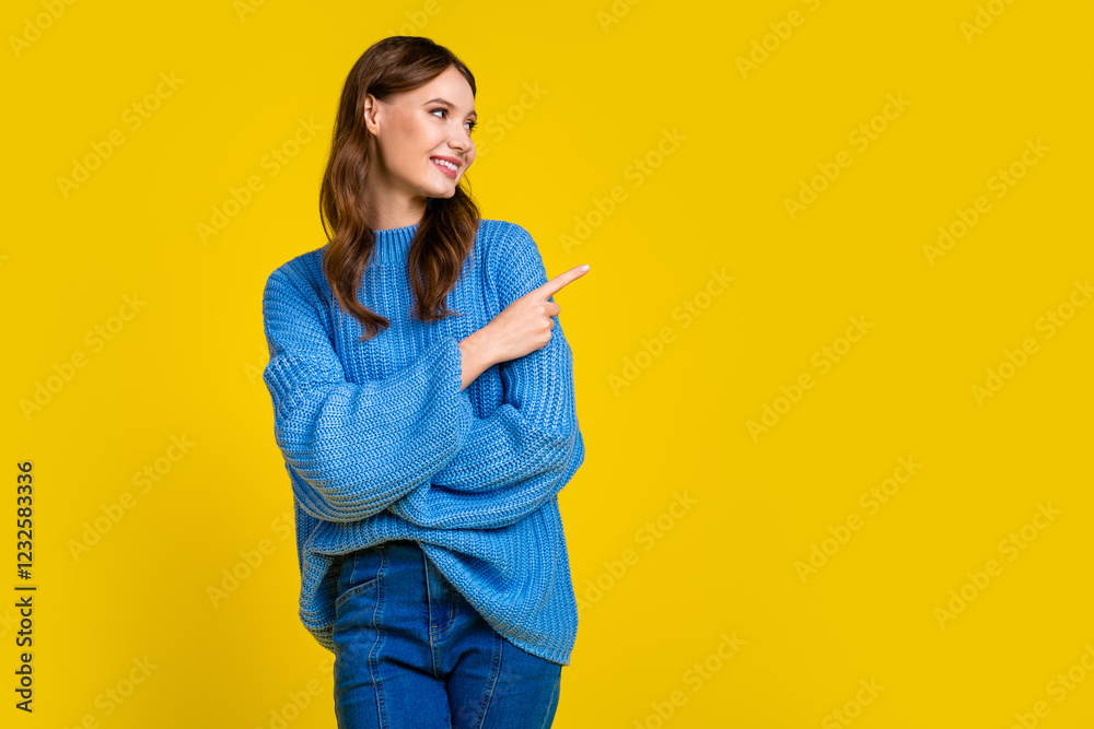 Casual girl in blue knitted sweater against yellow background pointing sideways with cheerful expression