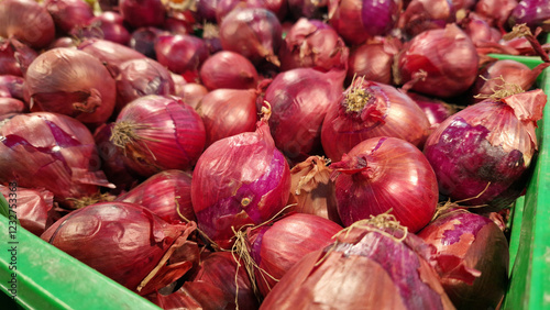 Red onion close-up in supermarket. Lots of red onions in plastic green box on market stall. Onions in green plastic box at farmers market. Onions for sale in store
