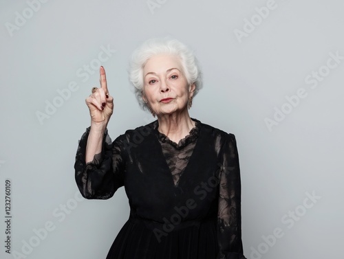 Elderly woman making a point while wearing elegant black dress against neutral background