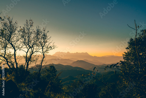 High-angle view of a beautiful warm sky in the evening as the sun sets. There is a view of Doi Luang Chiang Dao Mountain in the center, which has a unique shape. There are many trees in foreground.