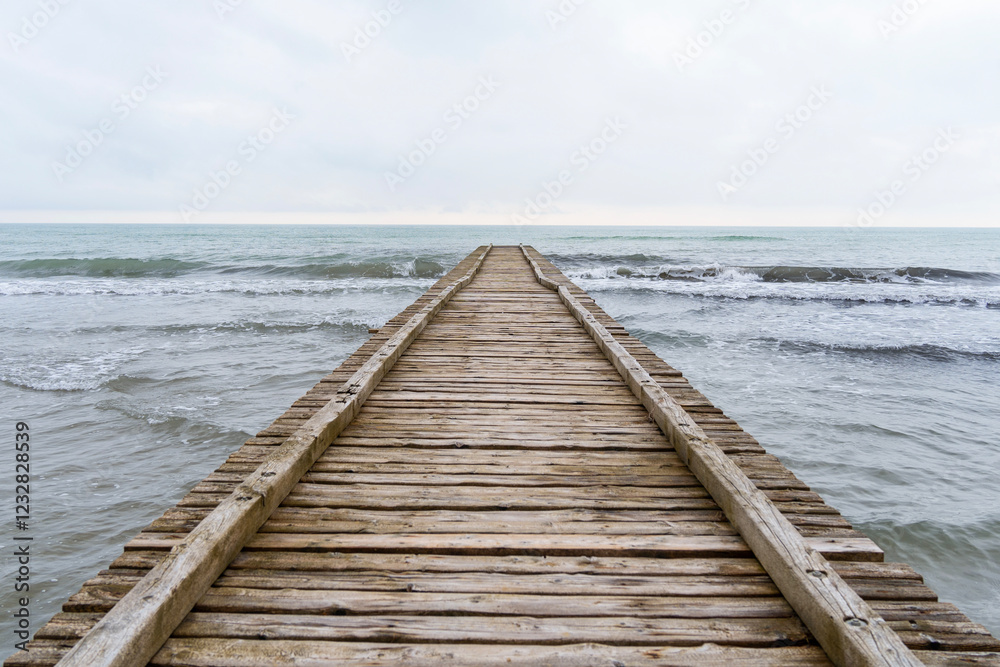 Fototapeta premium Wooden pier leading to the Adriatic Sea on a cloudy autumn beach in Italy