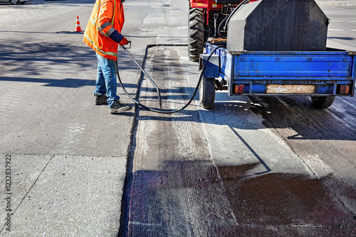 Obraz na płótnie Road worker applying sealant on freshly paved street at mid-morning in an urban area w salonie