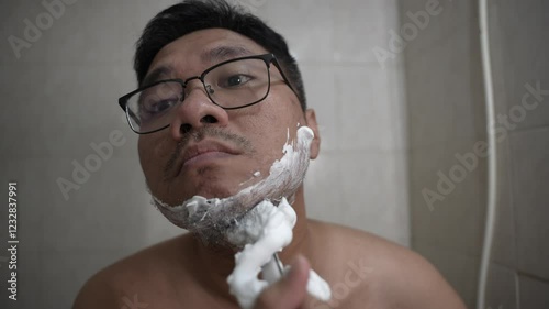 Young Asian man shaving his beard in the bathroom.
