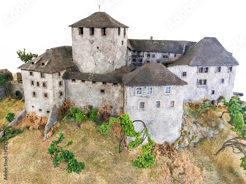 Detailed miniature model of a medieval fortress with stone walls, towers, and historical architecture, surrounded by realistic landscape elements, representing an ancient stronghold or castle diorama photo