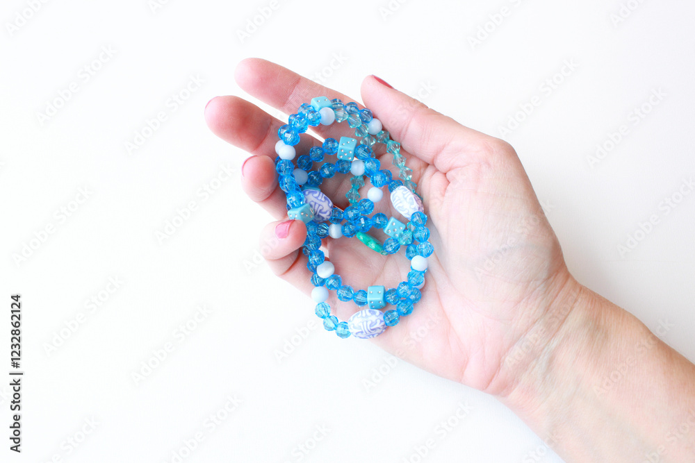 Close-up of woman's hand holding blue beaded bracelet. Handmade fashion accessory with acrylic beads. Elegant costume jewelry on white background with copy space. Perfect for jewelry design. Close-up of woman's hand holding blue beaded bracelet. Handmade fashion accessory with acrylic beads. Elegant costume jewelry on white background with copy space. Perfect for jewelry design.