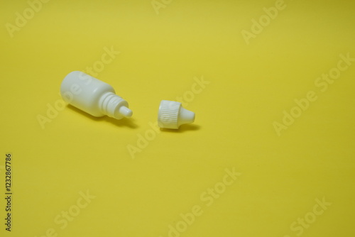 A white bottle, a vial for eye and nasal drops on a yellow background.