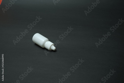 A white bottle, a vial for eye and nasal drops on a black background.
