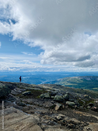 Hiker standing on rocky terrain with panoramic view of valleys and clouds under a bright sky in the mountains in Östersund, Sweden 