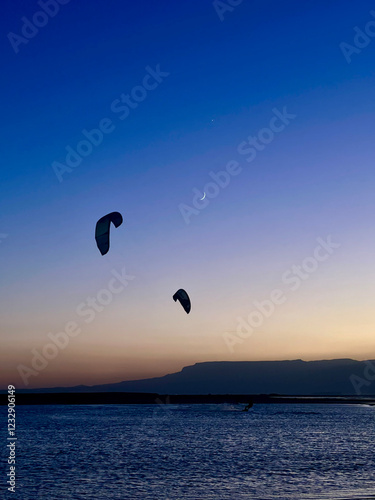 Silhouette of a kite surfer kiting on sunset with the moon view in the background in Egypt 