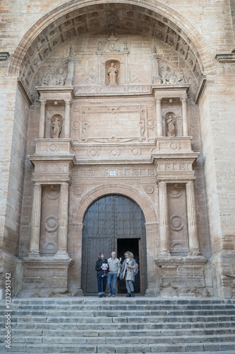 Three senior friends standing on the grand stone steps of a magnificent historic church facade during their cultural journey in Spain