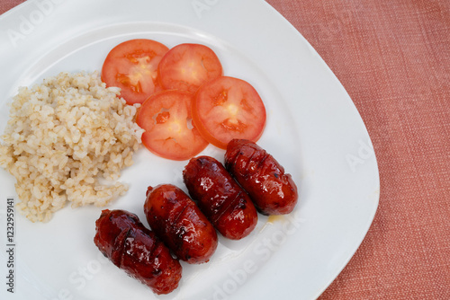 Sweet longaniza on a white plate with rice and tomatoes. photo