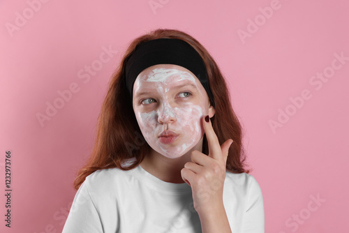 Teenage girl applying mask on her face with against pink background. Cosmetic product