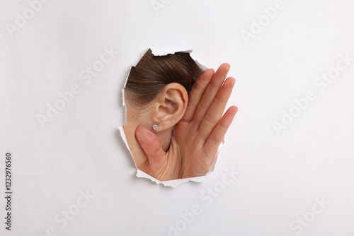 Εκτύπωση καμβά Woman showing hand to ear gesture through hole in white paper, closeup