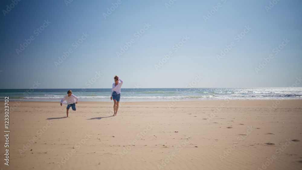 Happy boy running mother at sunny beach near ocean waves. Playful child woman Happy boy running mother at sunny beach near ocean waves. Playful child woman