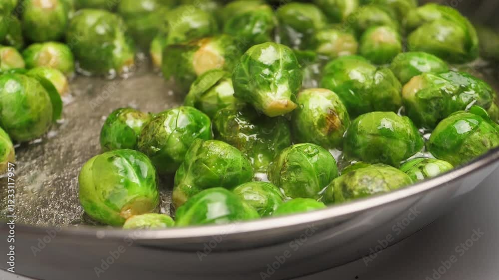 A cook uses a spatula to stir roasting brussel sprouts in a shiny frying pan and a generous amount of hot vegetable oil. Cooking a delicious vegetarian meal from vegetables. Healthy food and diet A cook uses a spatula to stir roasting brussel sprouts in a shiny frying pan and a generous amount of hot vegetable oil. Cooking a delicious vegetarian meal from vegetables. Healthy food and diet