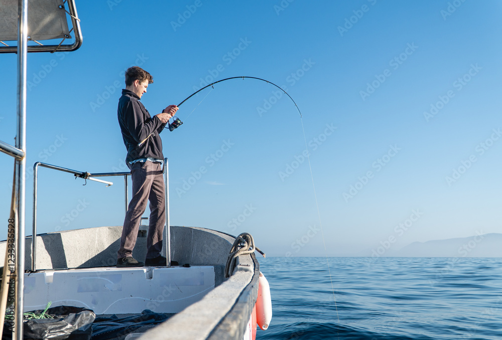 A young man focuses on casting his fishing line from a boat into the serene waters, immersed in the peaceful atmosphere of a calm day at sea.