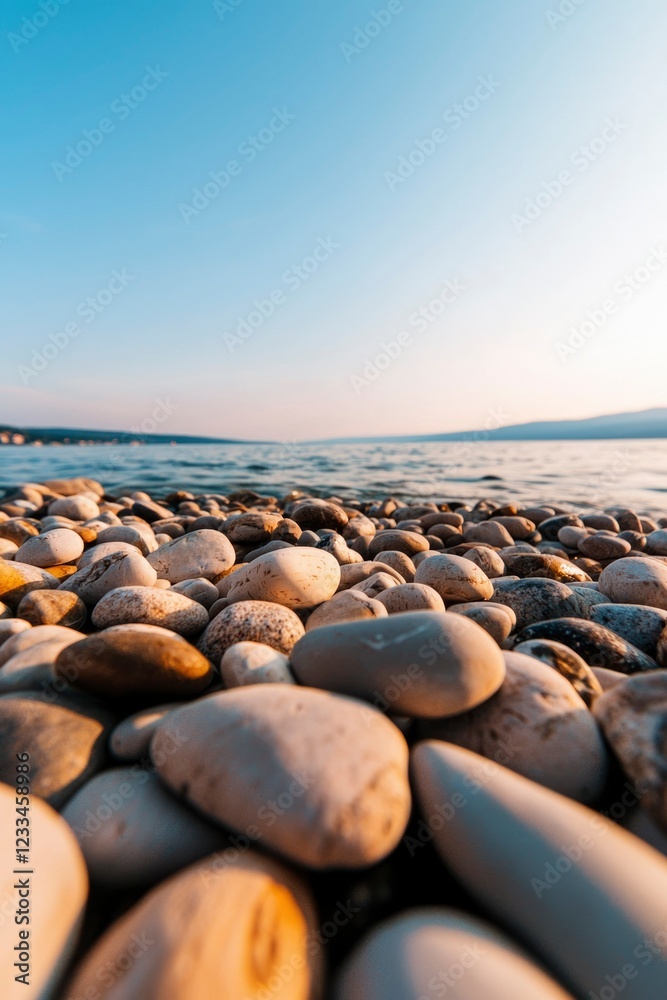 Smooth stones on a beach meet calm water under a blue sky Smooth stones on a beach meet calm water under a blue sky
