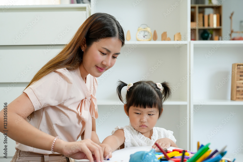 Asian teacher teaches children before enter kindergarten. Young girl practicing drawing with crayons while teacher guides learning. Interactive educational activity in supportive home environment. Asian teacher teaches children before enter kindergarten. Young girl practicing drawing with crayons while teacher guides learning. Interactive educational activity in supportive home environment.