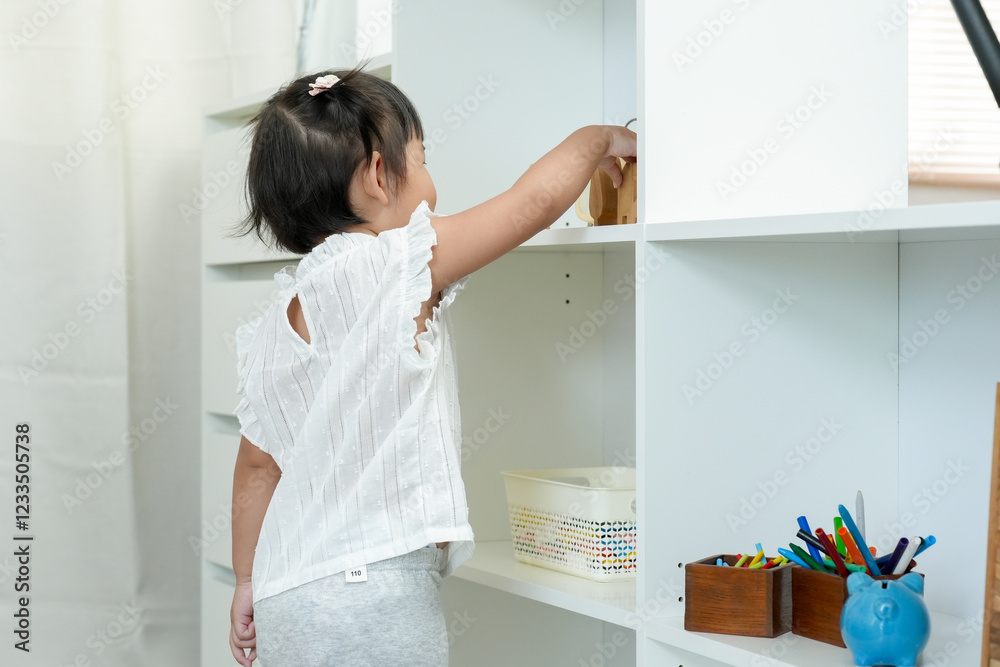 Asian Girls learn before going to school engaging in early childhood education activities at home organizing wooden toys on white shelf developing motor skills independence curiosity in learning Asian Girls learn before going to school engaging in early childhood education activities at home organizing wooden toys on white shelf developing motor skills independence curiosity in learning