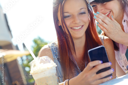 Cafe, phone and whisper with girl friends drinking ice coffee outdoor in park together for break. App, relax and secret rumor with women at table in nature for bonding, gossip or text message