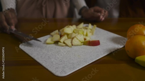 Close-up of two multiracial women in casual clothes peel banana cutting apple and smiling with love in a modern kitchen at home. photo