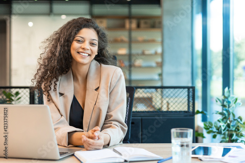 Happy smiling young African American professional business woman at workplace working on laptop computer in office, looking at camera
