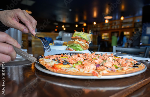 Obraz na płótnie Hands holding forks and cutting a salmon pizza. Unrecognizable people in the restaurant. Alaska. w salonie