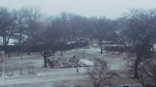 A video wide shot of a man running in the park while snow is outside in the morning.