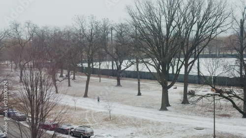 A video wide shot of a man walking in the park while snow is outside in the morning.