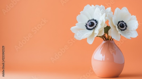 Two white anemone flowers elegantly arranged in a peach fuzz color vase against a minimal background. photo