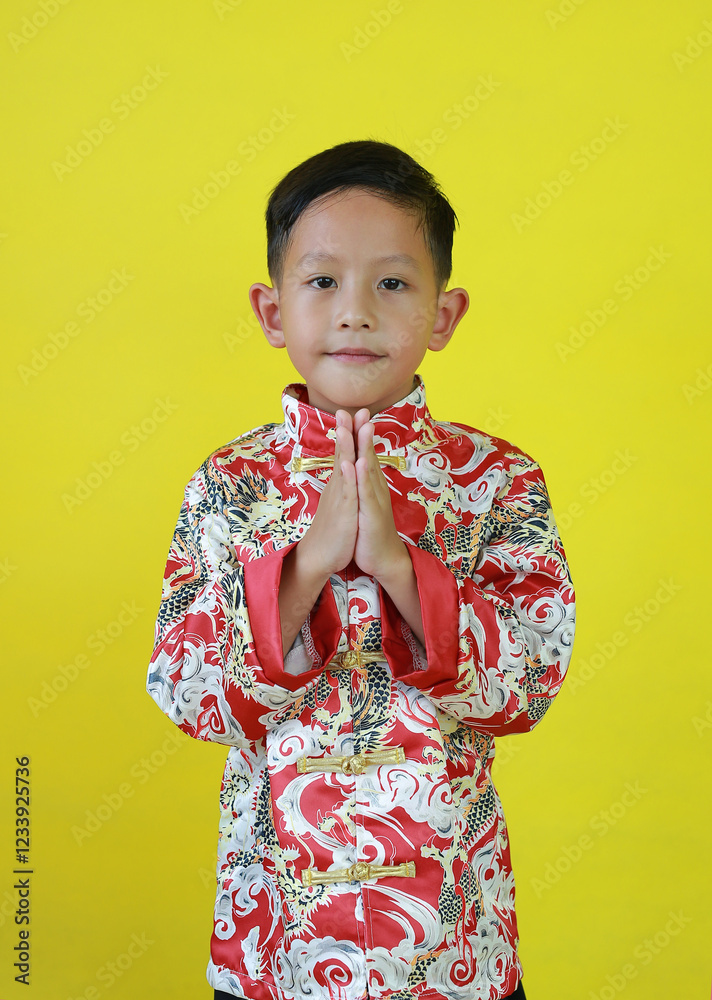 Chinese boy in traditional dress with praying gesture isolated on yellow background celebration for Chinese New Year. Chinese boy in traditional dress with praying gesture isolated on yellow background celebration for Chinese New Year.