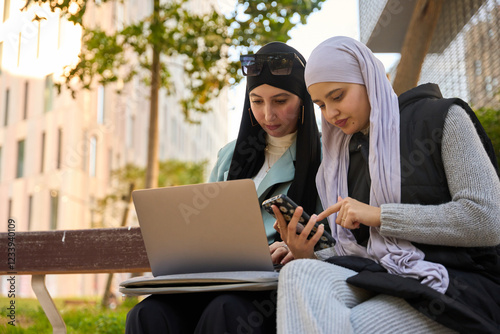 Two muslim businesswomen working outdoors with laptop and smartphone photo