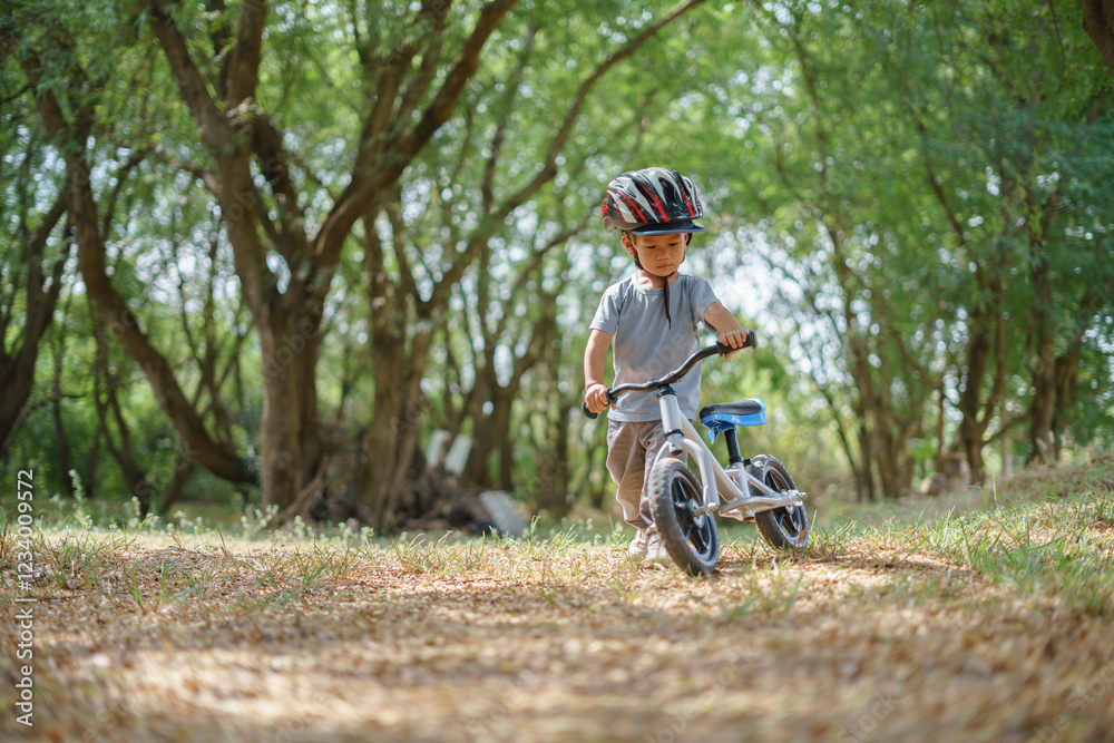 Young Thai child wearing a helmet, walking with a balance bike through a sunlit forest, exploring nature and adventure. Young Thai child wearing a helmet, walking with a balance bike through a sunlit forest, exploring nature and adventure.
