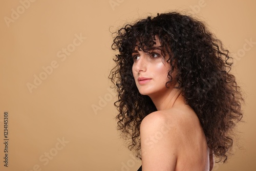 Beautiful young woman with long curly hair on beige background. Space for text