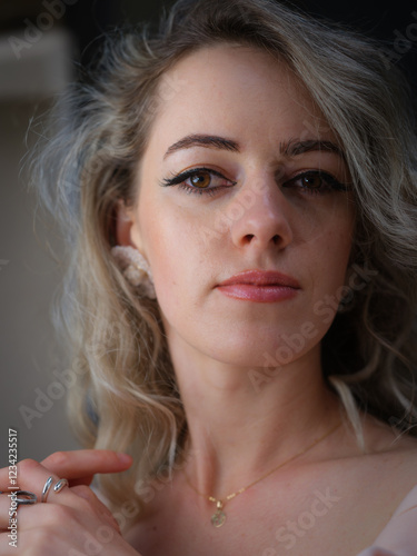 A close-up portrait of a stylish woman with wavy blonde hair, silver rings, and subtle makeup, gazing thoughtfully to the side with elegance against a dark background